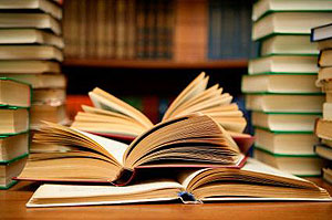 Libros abiertos en un escritorio de biblioteca con más libros apilados alrededor.